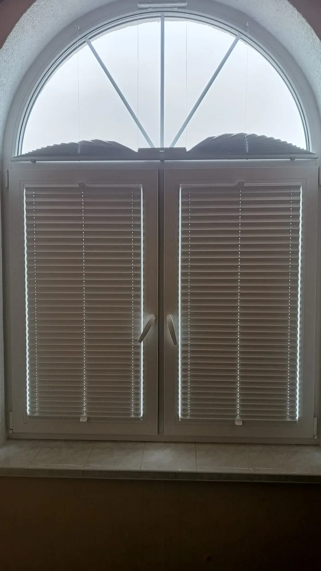 Realizacja M&G: białe plisy na oknie z naświetlem górnym. Dolne plisy zasłaniają szyby, górna plisa w kształcie wachlarza jest w pozycji złożonej.